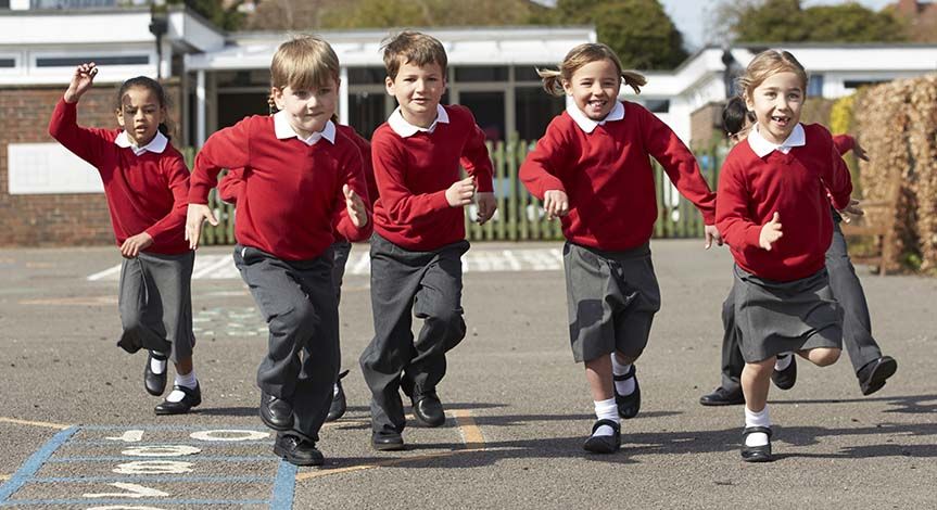 Kids running in the school yard wearing red shirt and grey pant uniforms 